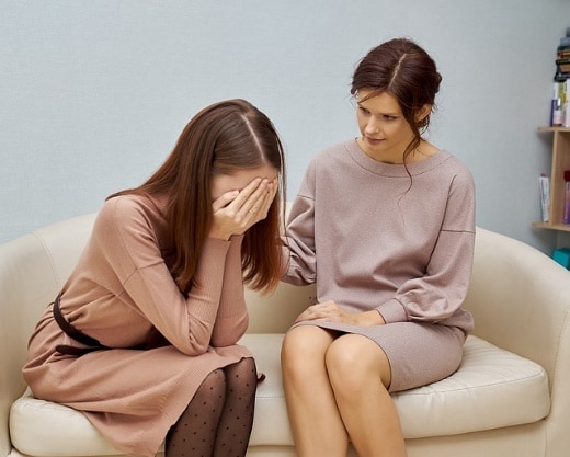 A person sitting on a couch with another person looking at her Description automatically generated with low confidence