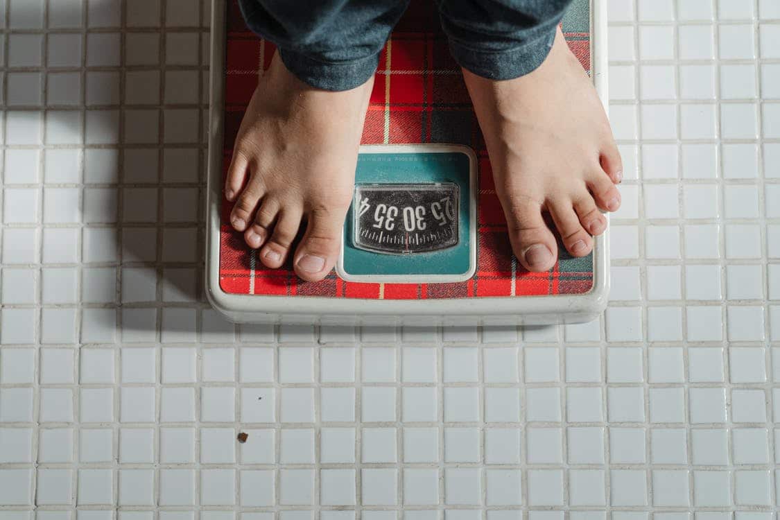 From Above Crop Anonymous Barefoot Child In Jeans Standing On Weigh Scales On Tiled Floor Of Bathroom