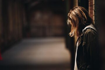 Woman Leaning Against A Wall In Dim Hallway